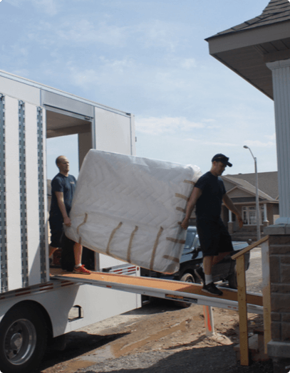 Two movers from First Rate Movers safely carry a mattress off of a moving truck