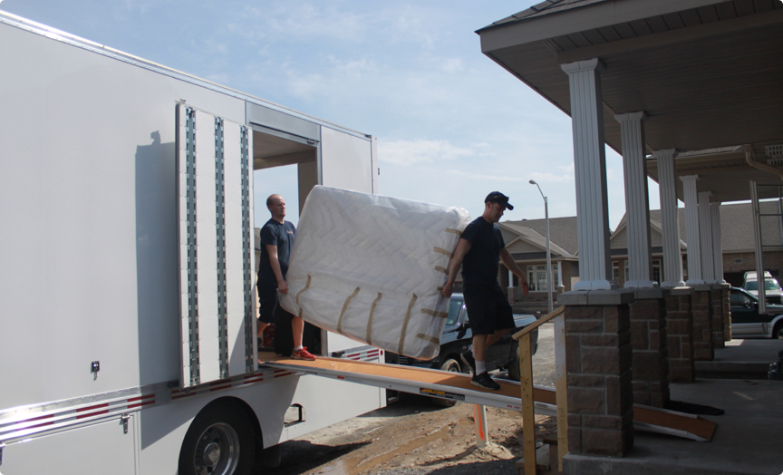 Two movers from First Rate Movers unload a mattress from a moving truck